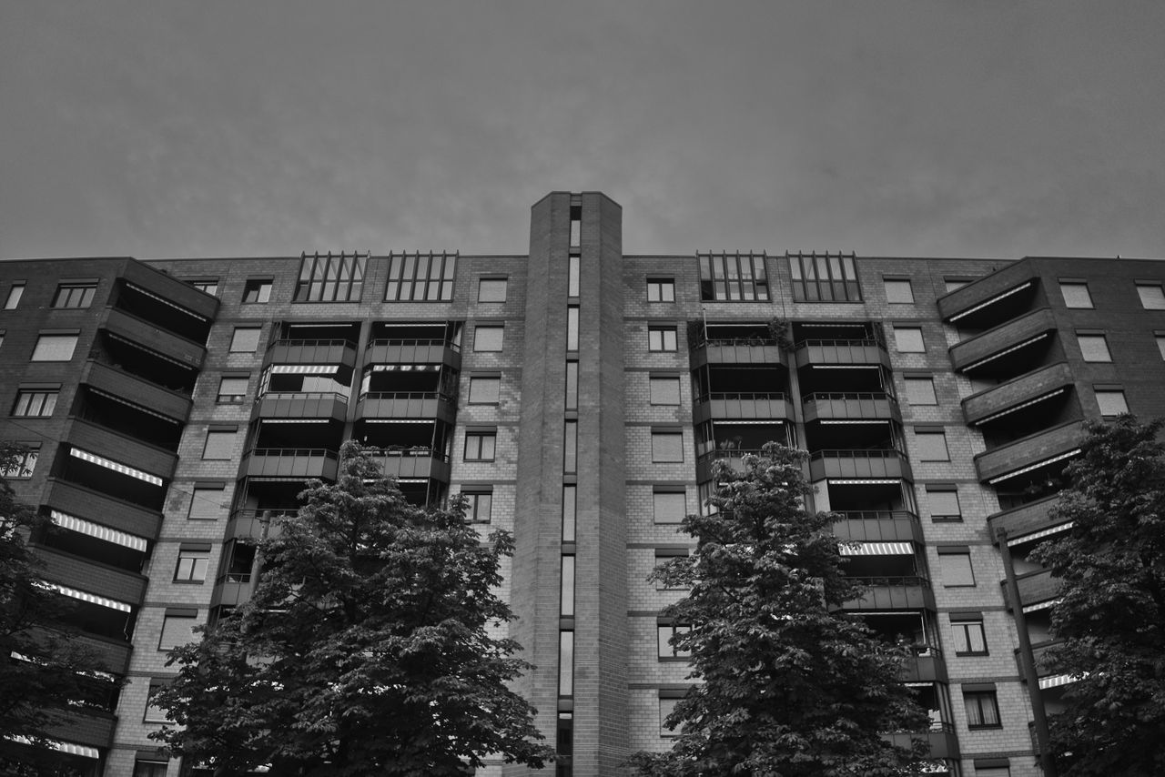 Mastering the First Impression: Your intriguing post title goes here Black and white photo of a modern apartment building facade with trees.